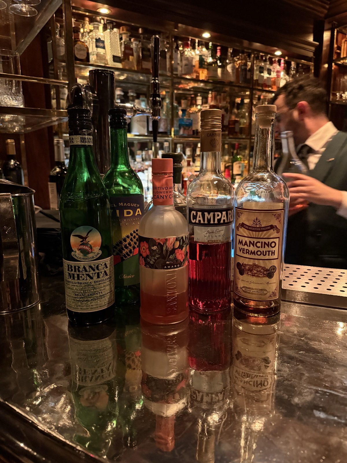 The Bloomsbury Hotel, London: The Bloomsbury Club Bar, bottles lined up on the bar for a tasting: Branca Menta, Del Maguey Vida mezcal, Amaro Santoni, Campari, Mancino vermouth, the bartender behind, 26 Sep 2026, 21:02